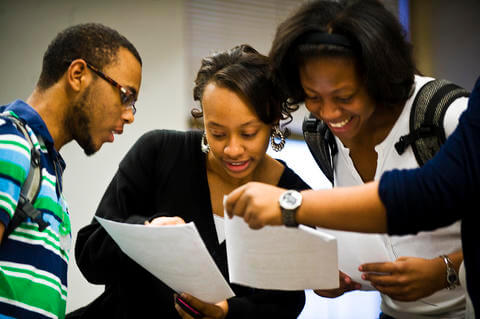 Three african-american people looking over informational papers. Two well-dressed women and one young man with glasses