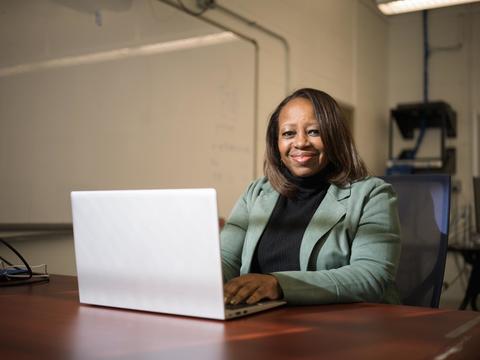 Professor Yanick Rice Lamb sits at desk with laptop